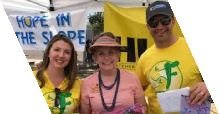A group of smiling volunteers standing in front of a yellow "Hope in the Slope" banner at a Sunnyslope community event.
